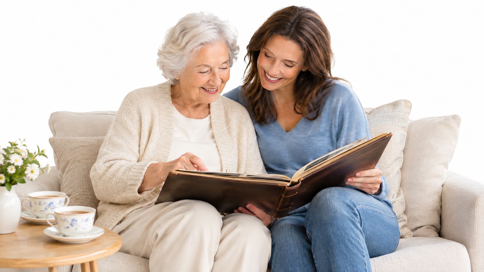 An elderly woman and her daughter sitting on a sofa looking at an old photo album together.
