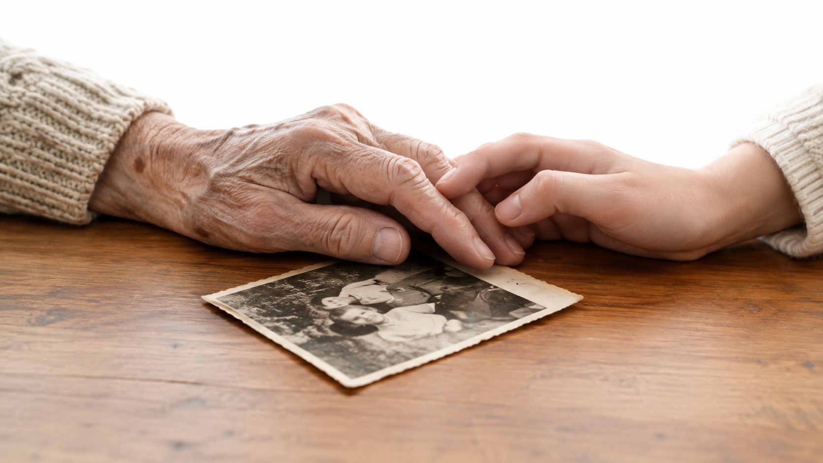 An elderly person's hand resting gently on a young person's hand over a nostalgic black and white photograph.