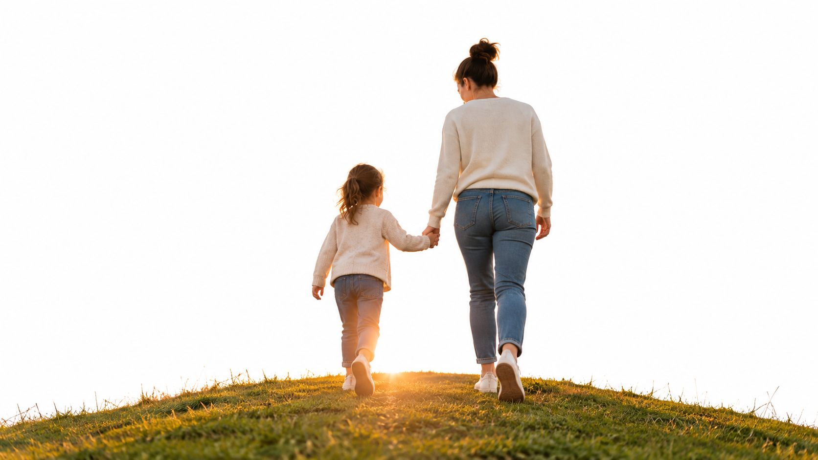 A mother and her young daughter holding hands while walking up a grassy hill at sunset