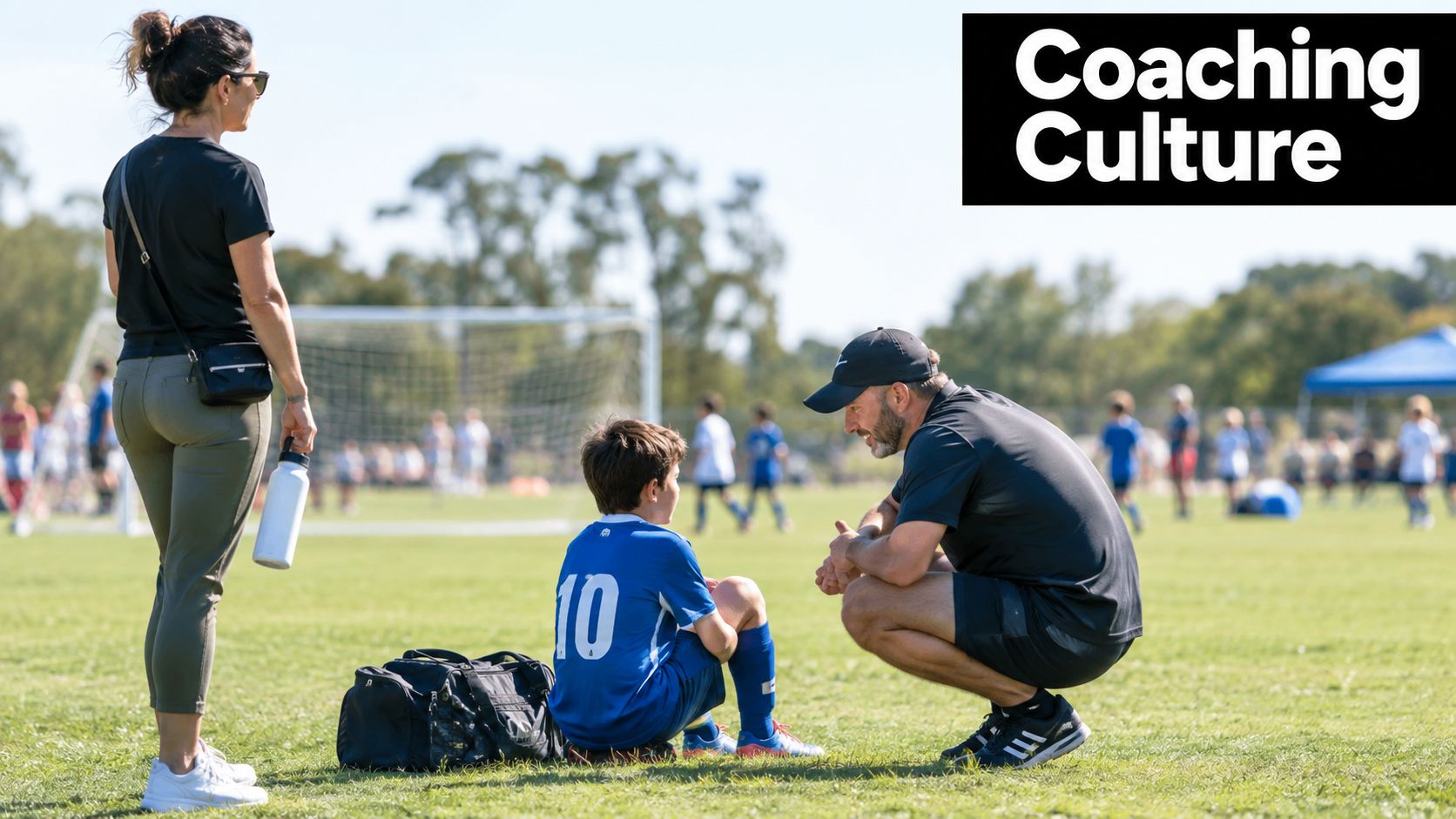 A soccer coach kneeling down to have a conversation with a young player on the field.