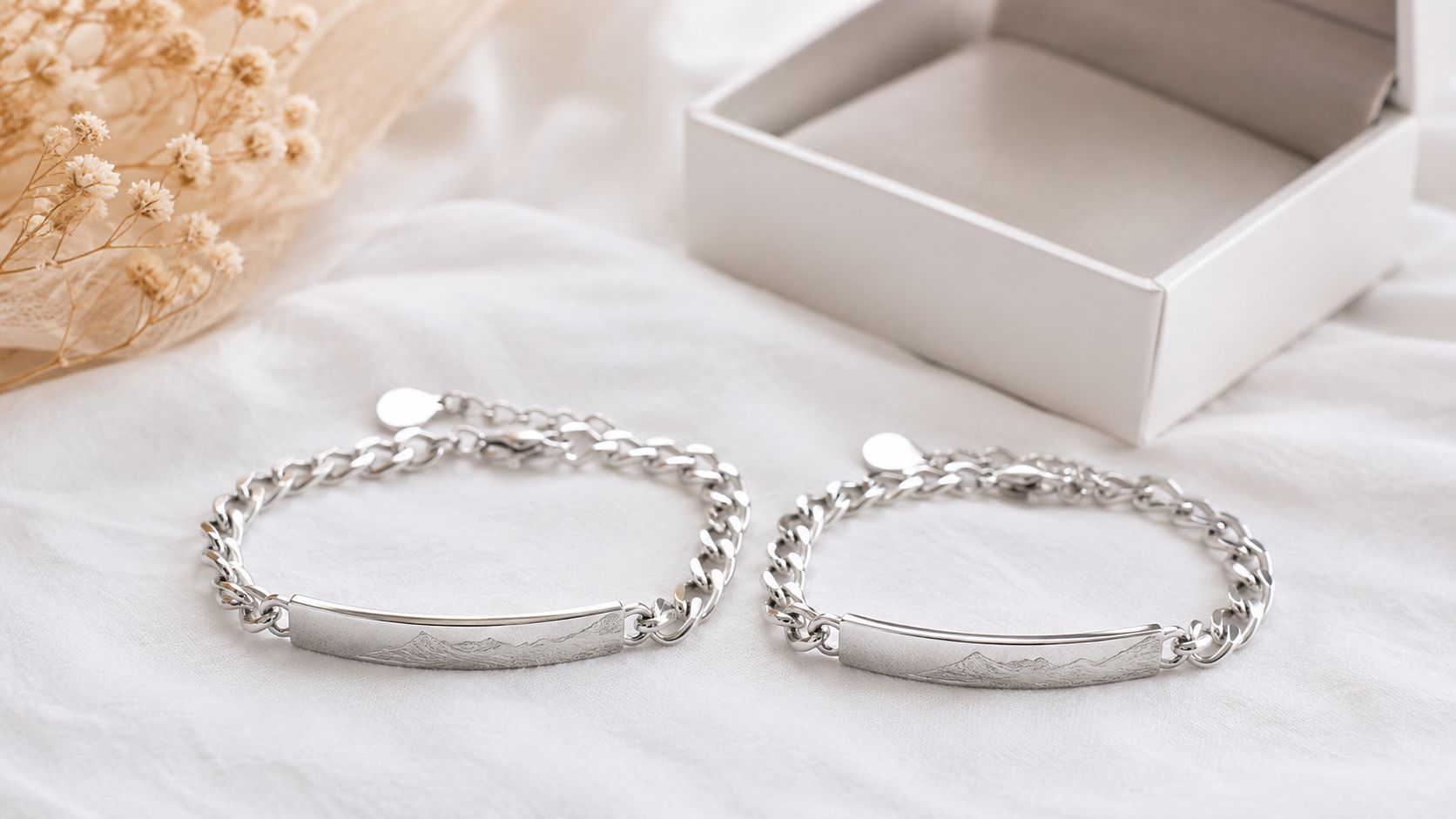 Zwei silberne Armbänder mit eingravierten Bergmotiven liegen auf einem hellen Stoff neben einer passenden Schmuckschatulle.