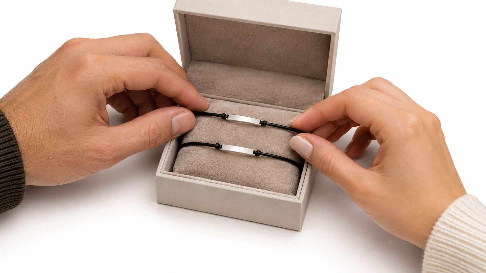 To stilige armbånd med anheng i sølv presenteres av to personer i en elegant gaveeske.