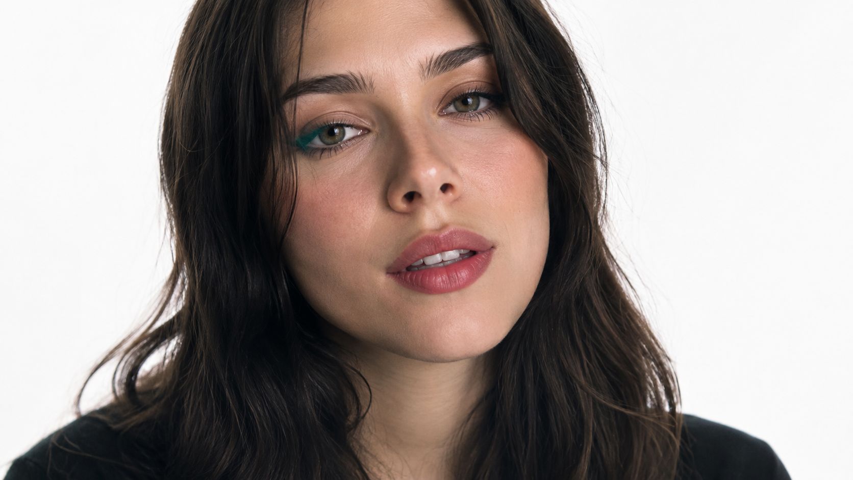 A close-up portrait of a woman with long dark wavy hair looking directly at the camera.