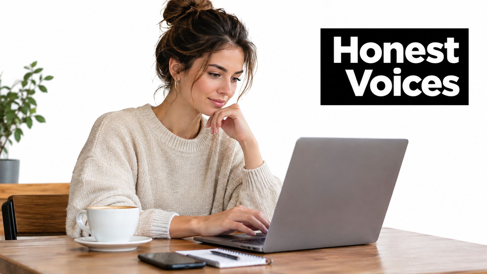A woman with her hair in a bun working on a laptop at a wooden table.
