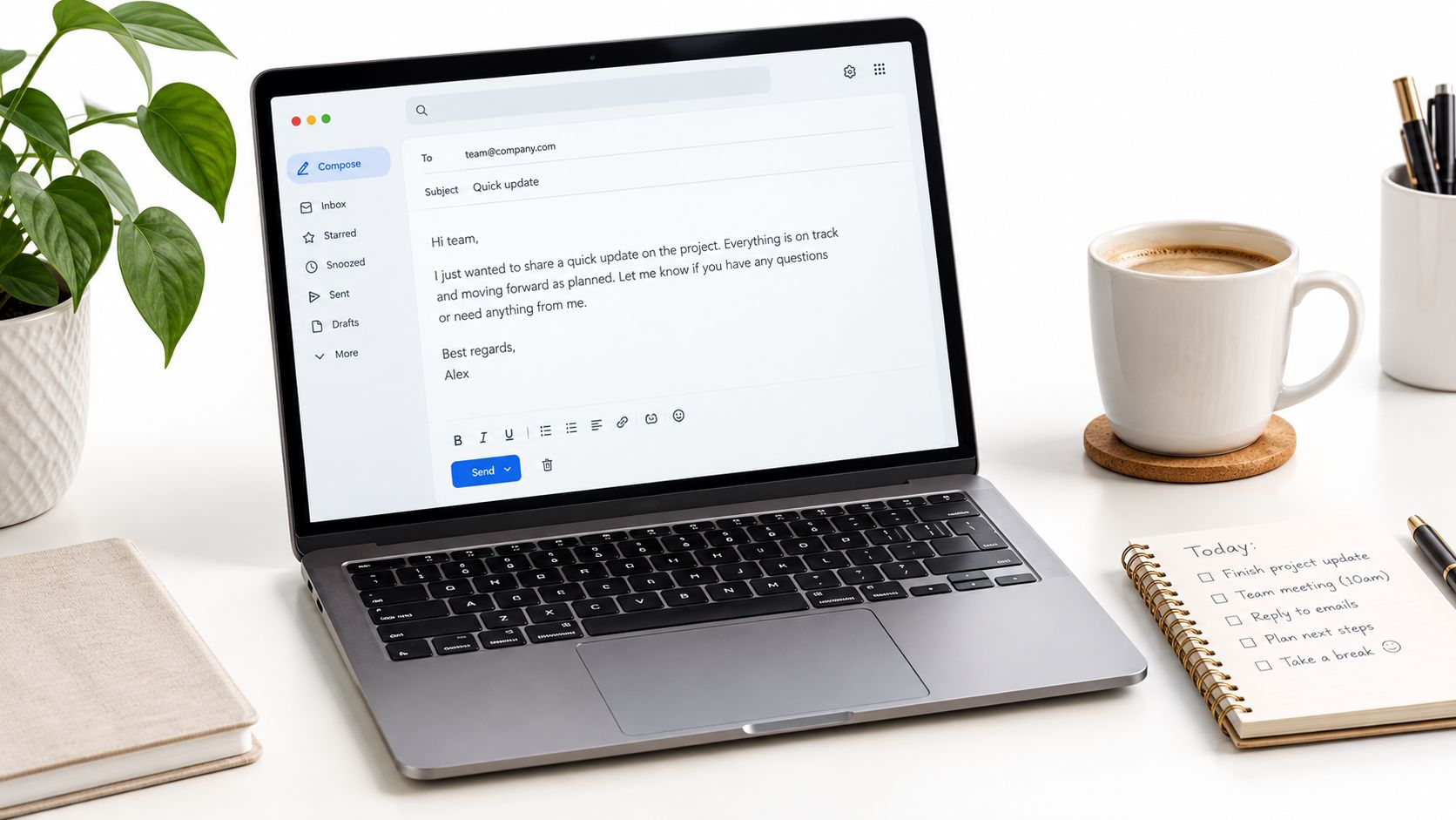 A modern laptop on a desk showing an email composition window next to a coffee and notepad.