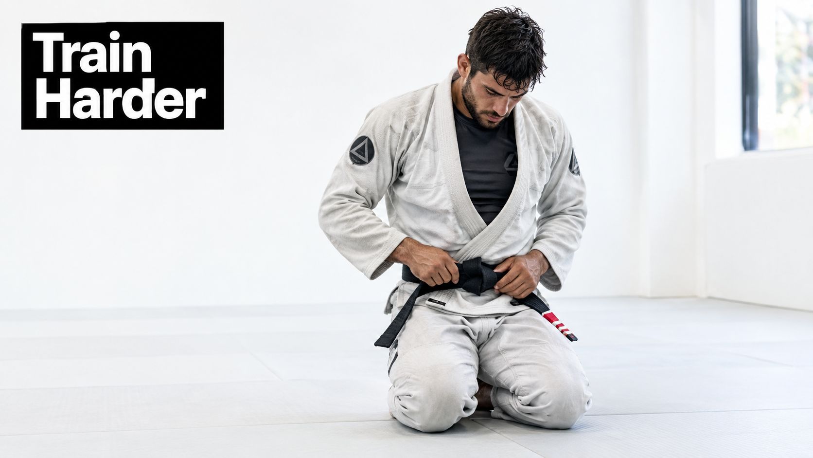 A martial artist in a white gi and black belt kneeling on a gym mat.