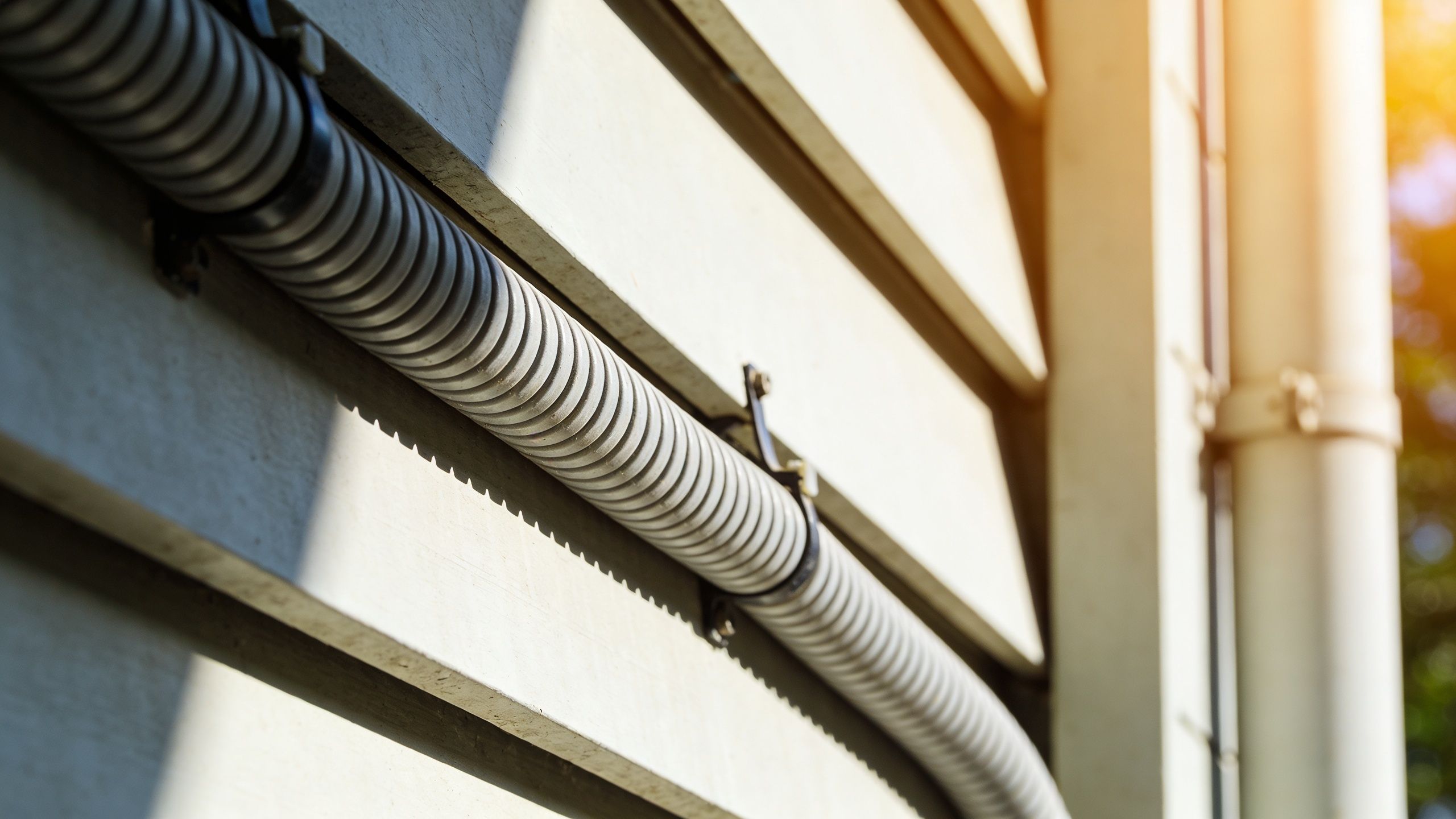 A Close-Up View Of A Grey Corrugated Electrical Conduit Pipe Mounted Horizontally On A Siding Wall