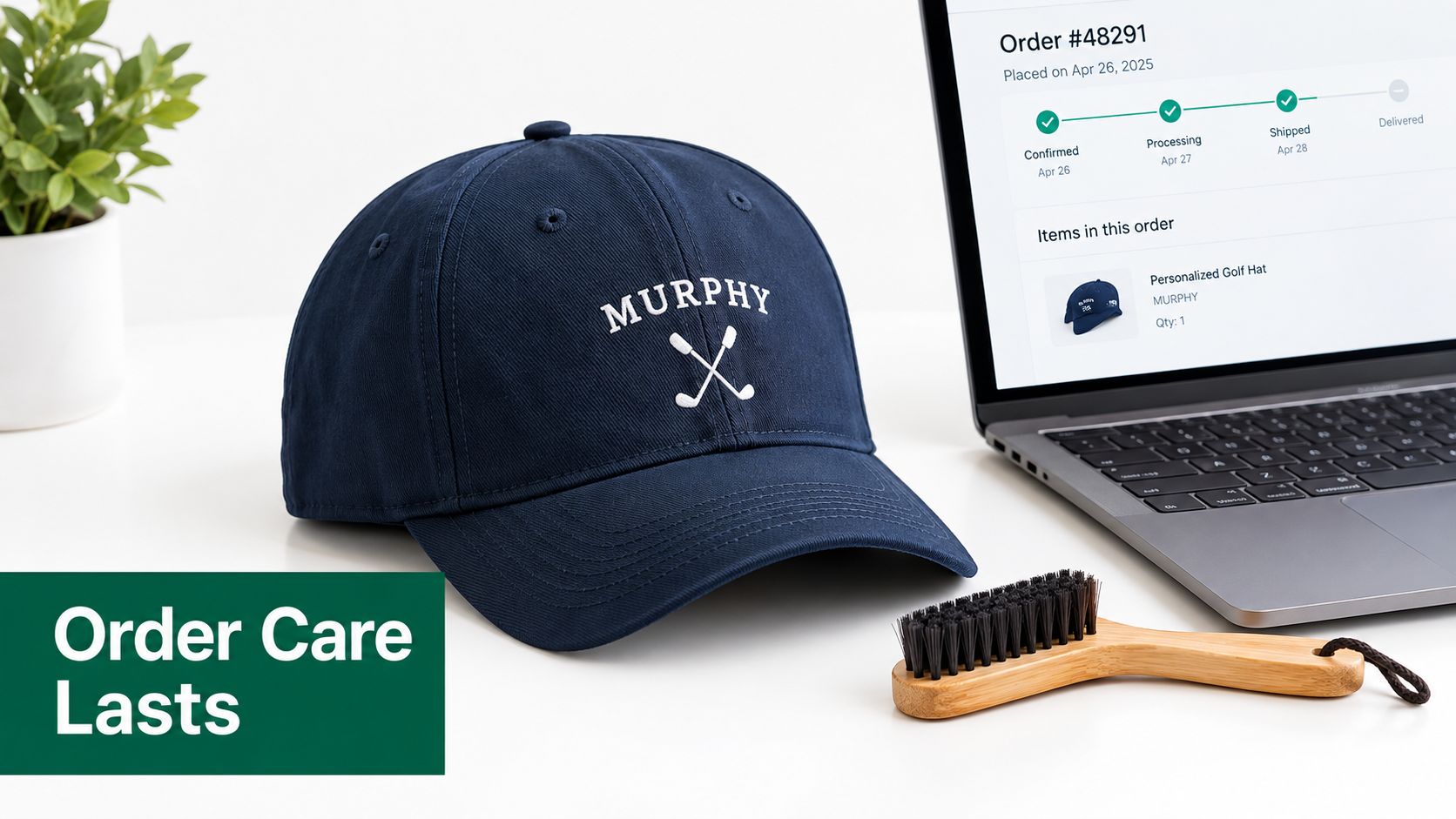 A navy blue personalized golf hat sits on a white desk next to a laptop and brush.