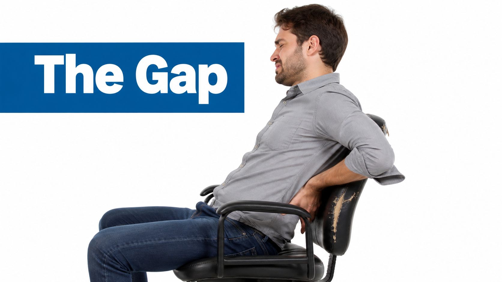 A man in a grey shirt experiencing back pain while sitting in a worn black office chair.