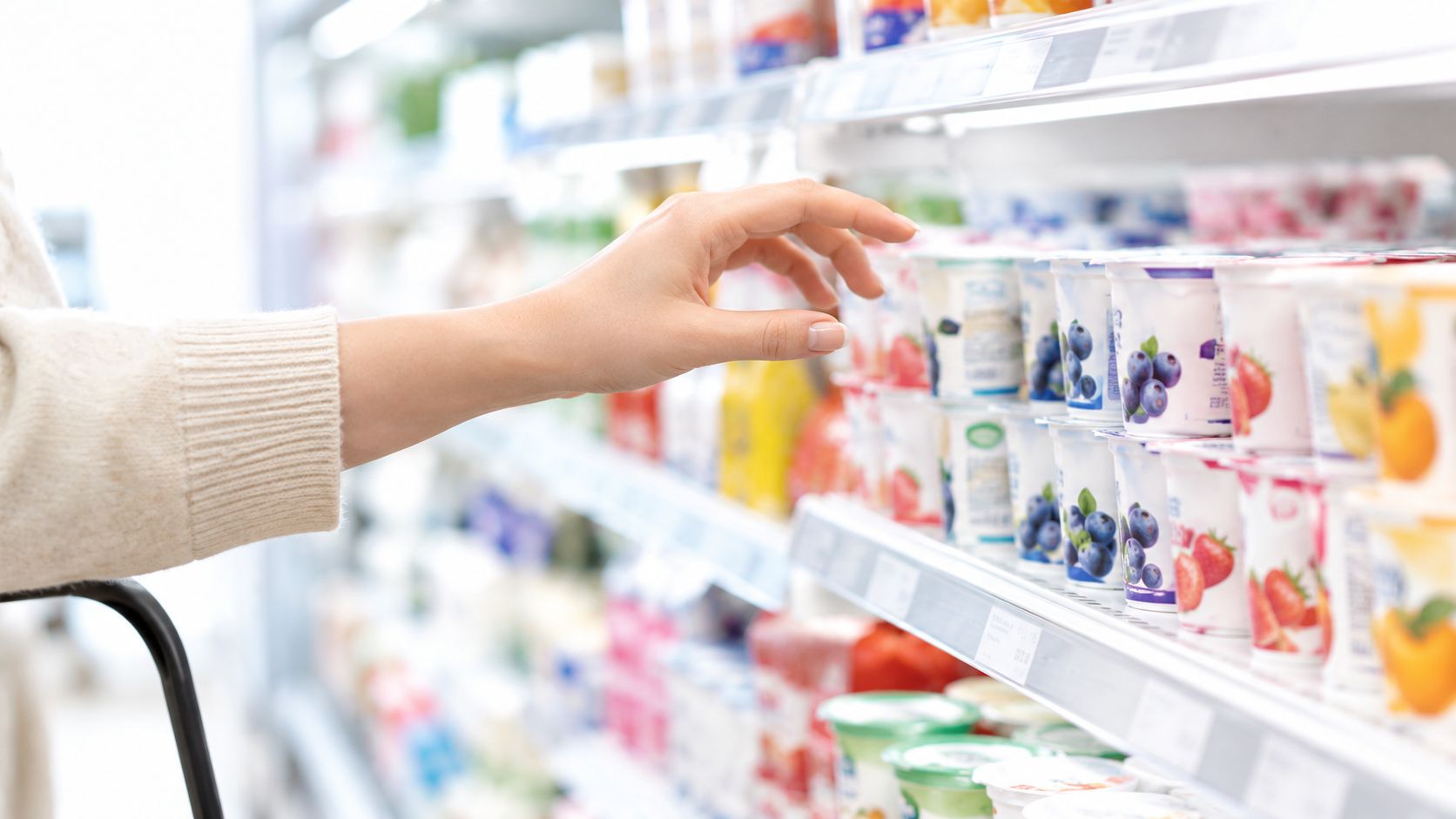 Eine Person greift im Supermarkt in das Kühlregal, um einen Joghurt aus der Auswahl zu wählen.