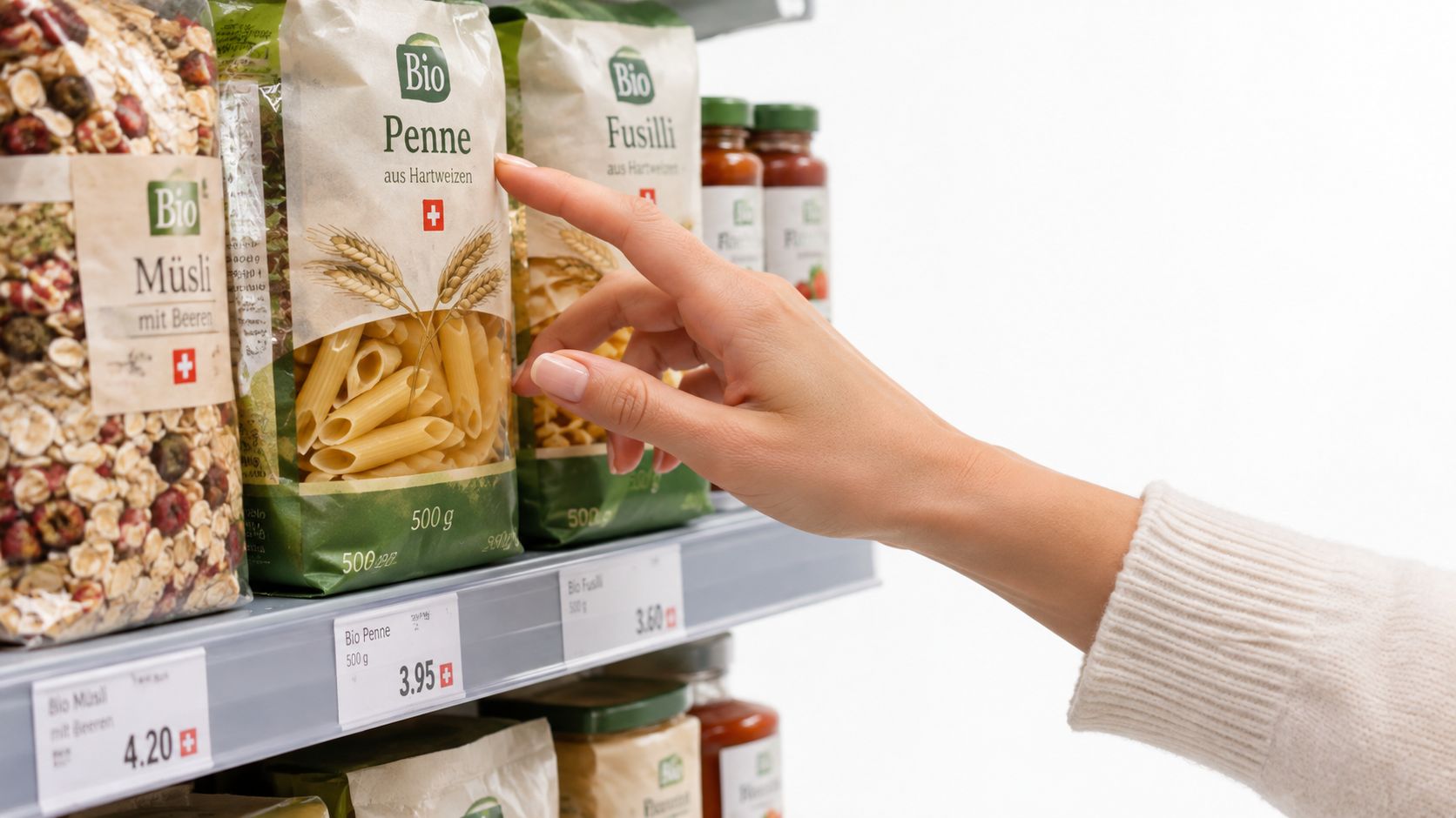Eine Hand greift nach einer Packung Bio-Penne-Nudeln in einem Supermarktregal für einen gesunden Einkauf.