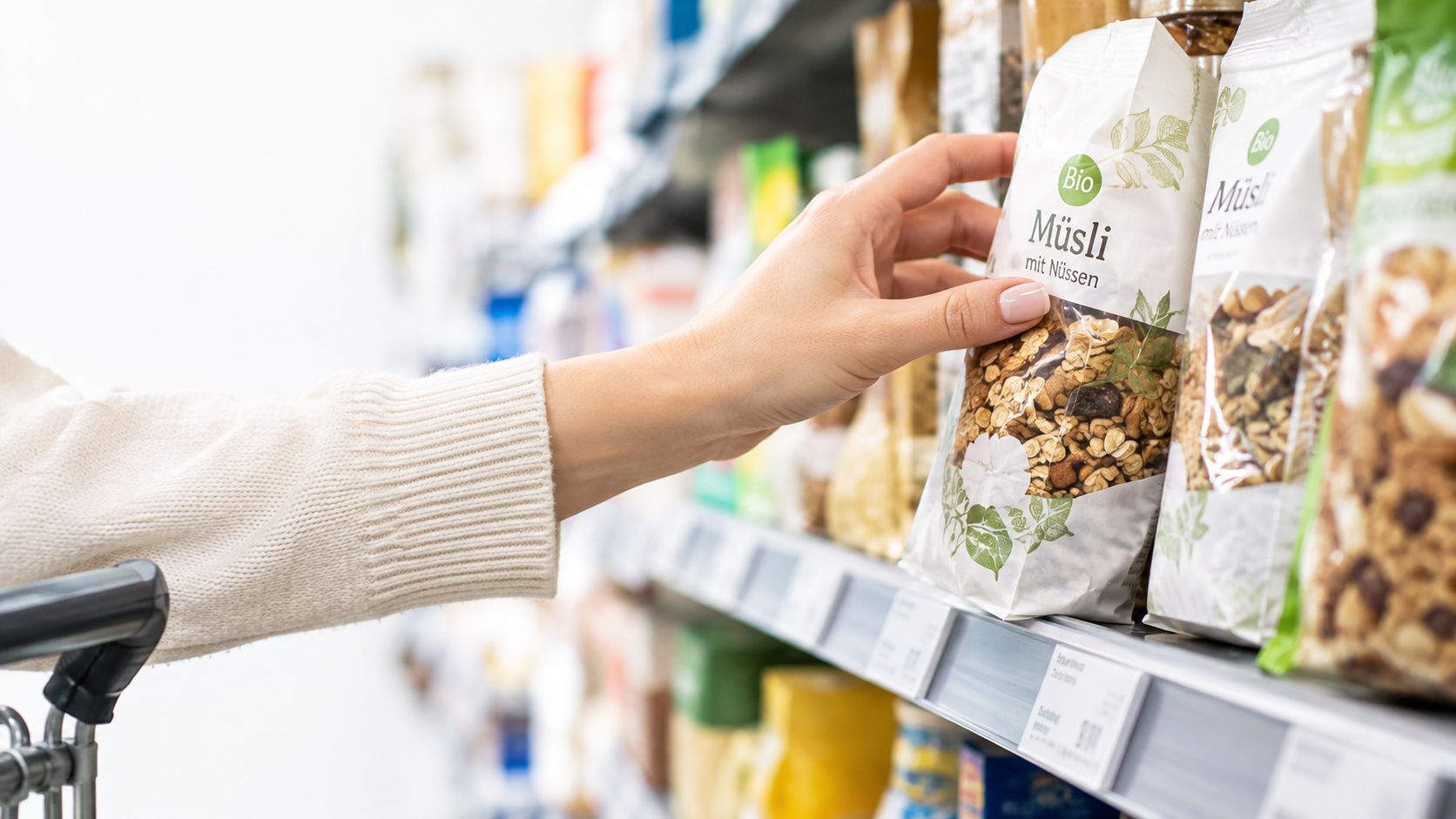 Eine Hand greift nach einer Packung Bio-Müsli mit Nüssen im Regal eines Supermarktes beim Einkaufen.