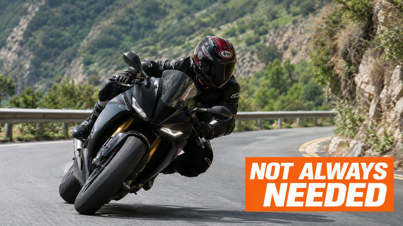 A motorcyclist in professional racing gear leans into a sharp turn on a winding mountain road.