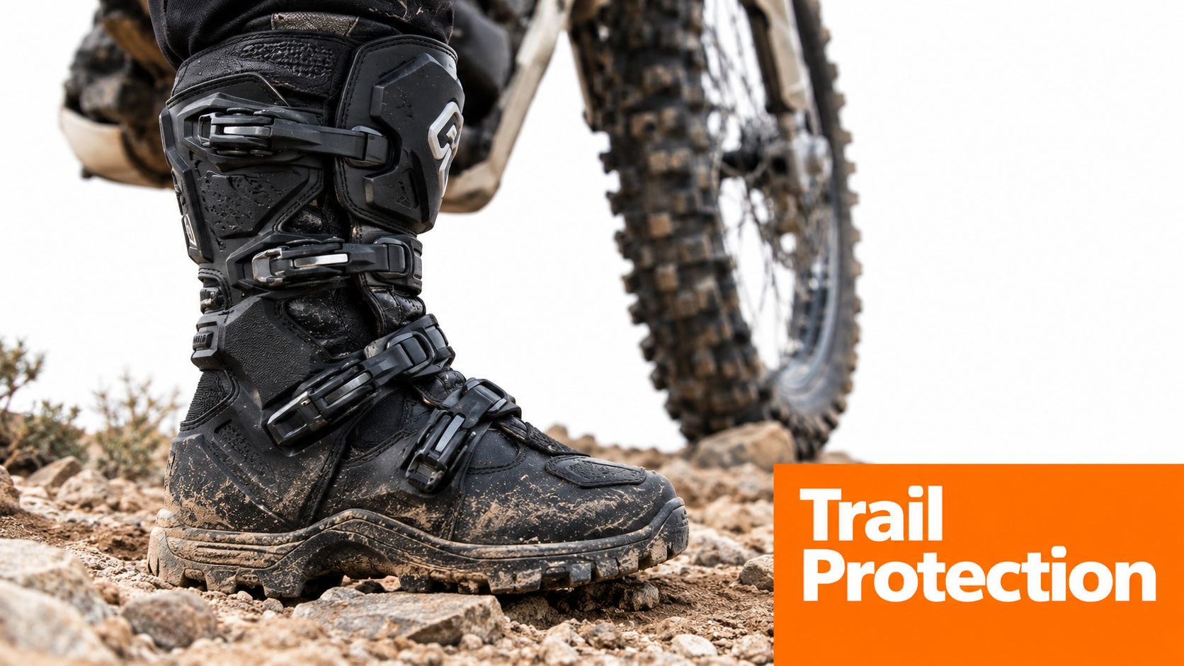 A close-up shot of a muddy motorcycle boot standing on a rocky dirt trail next to a bike