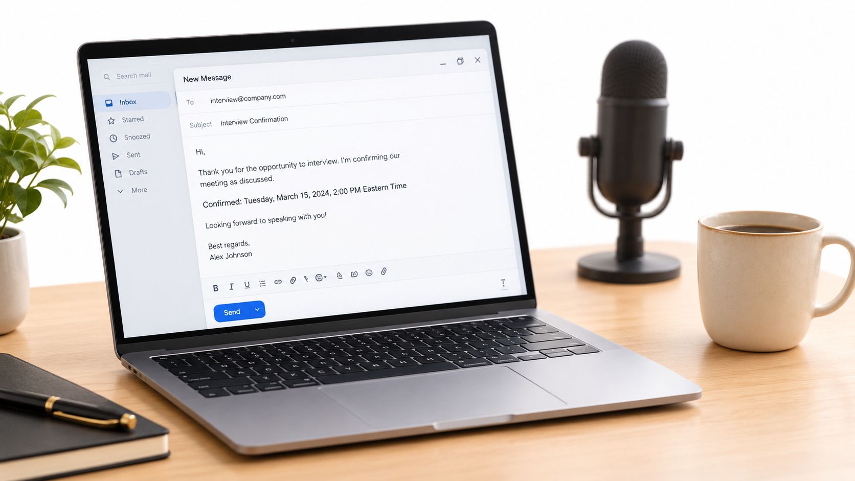 A modern laptop on a wooden desk showing an interview confirmation email draft, accompanied by a microphone and coffee.