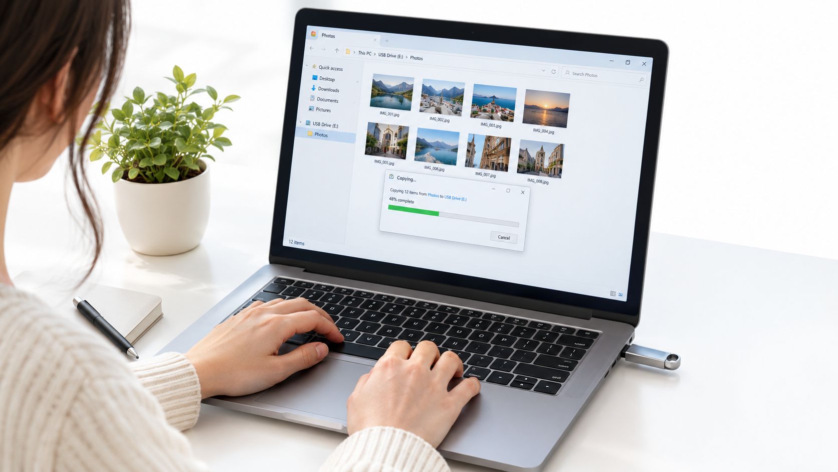 A woman using a laptop to transfer photo files from her computer to a USB flash drive.