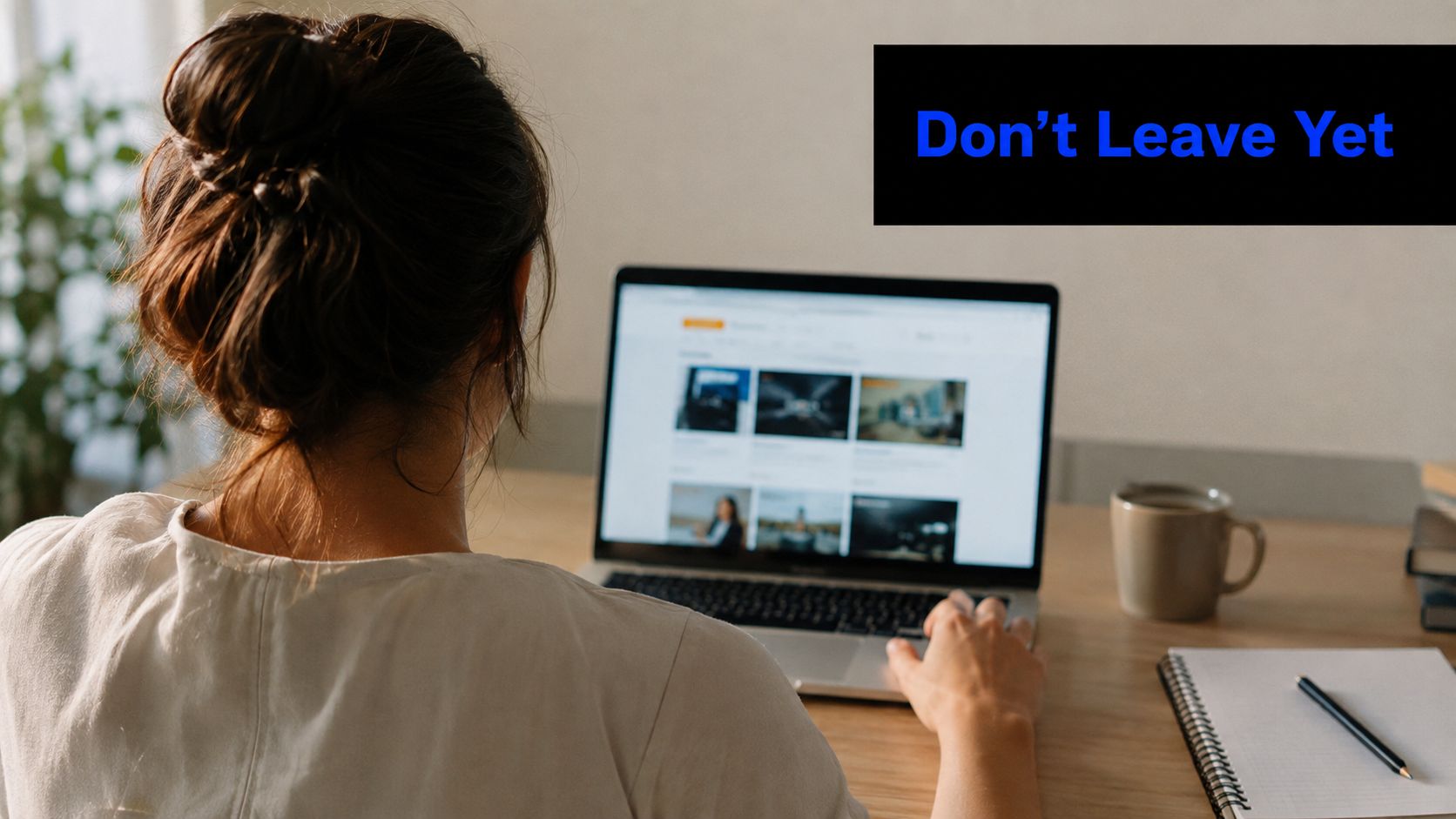 A woman working on her laptop at a desk with a coffee mug and notebook nearby.
