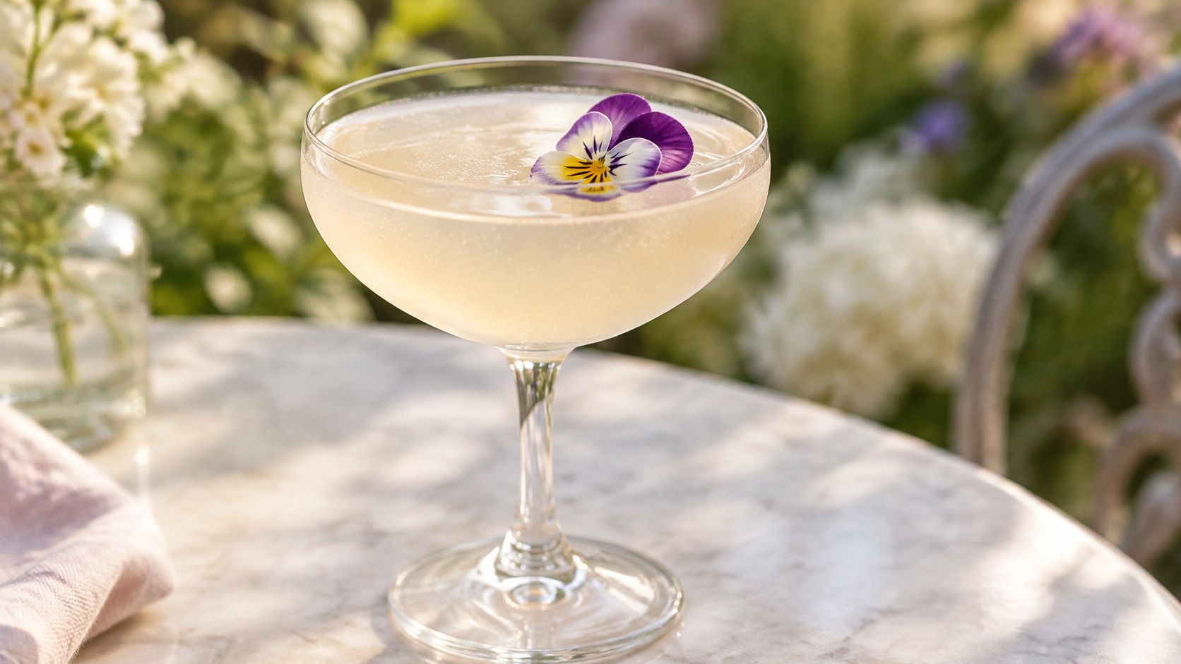 A pale cocktail in a coupe topped with a purple and yellow pansy-style flower.