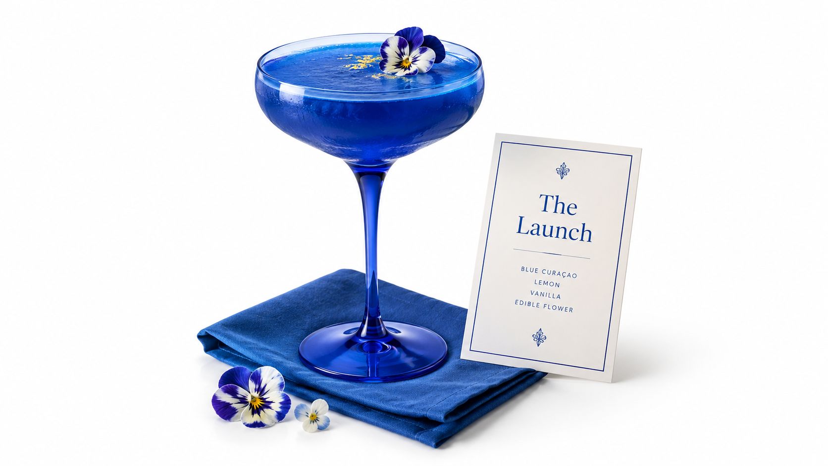 A blue themed cocktail with a flower garnish beside a menu.