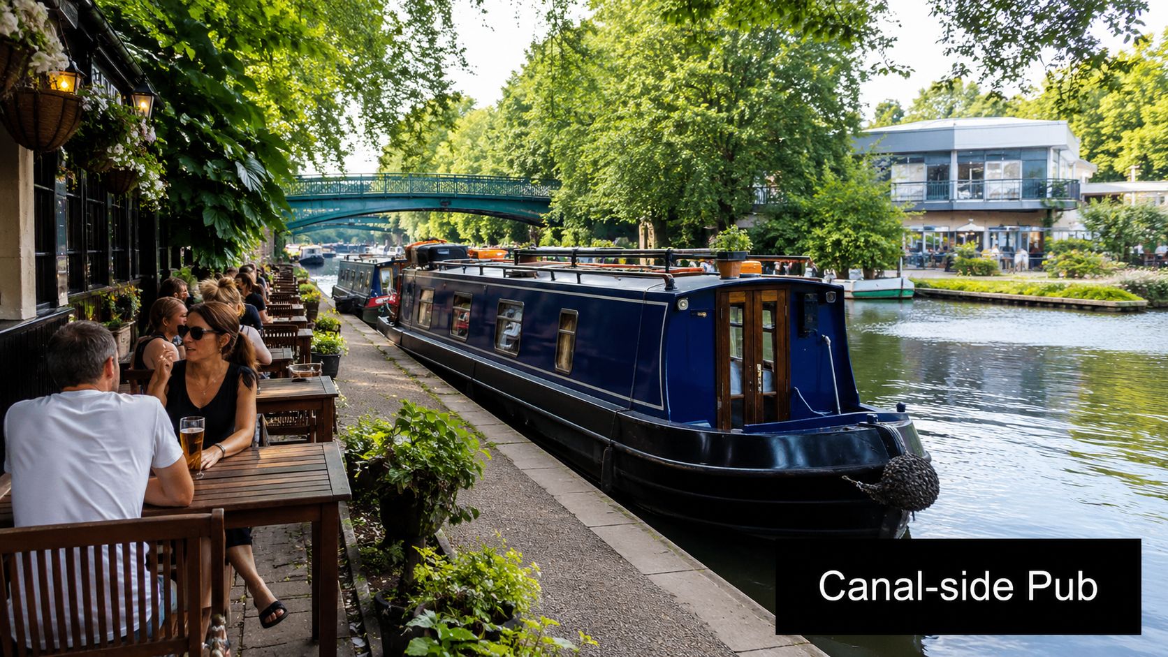 A picturesque canal-side pub in London with people dining on a sunny outdoor terrace by boats.