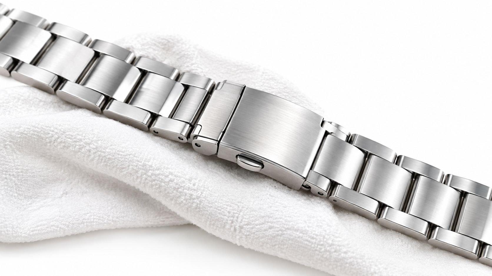 A close-up view of a stainless steel watch bracelet resting on a soft white cloth fabric.