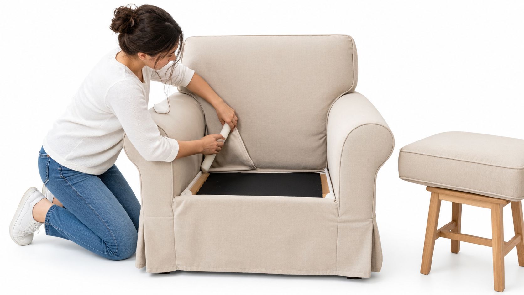A young woman assembling a beige Ektorp IKEA armchair while kneeling on the floor next to a stool.