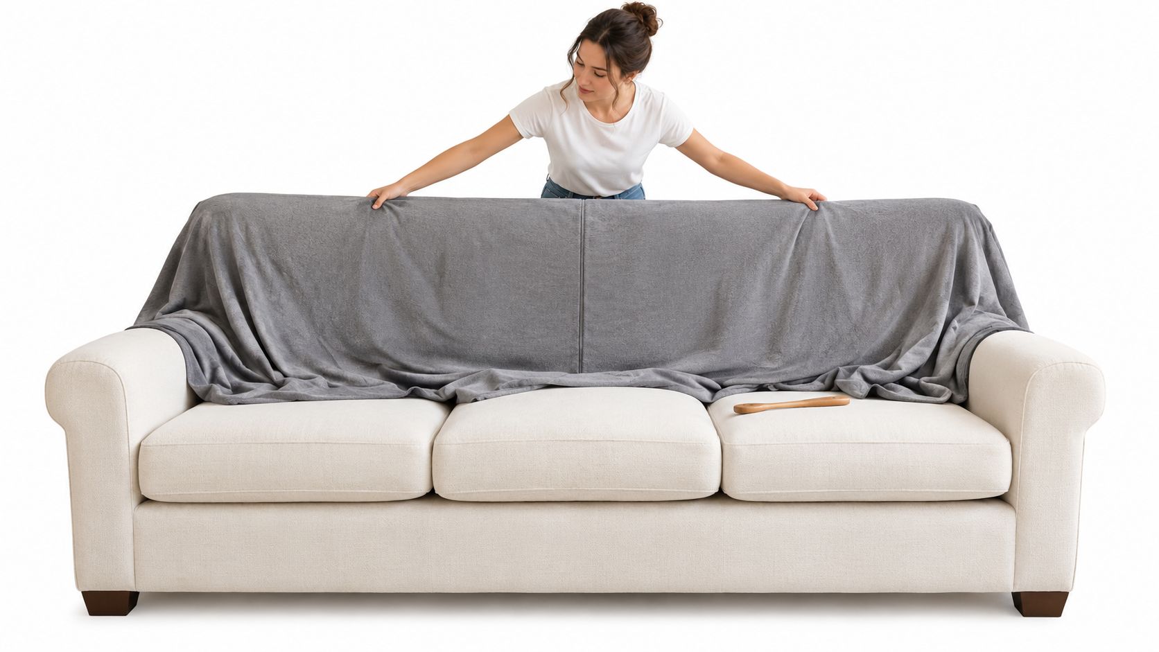 A woman carefully adjusting a soft gray fabric cover over a white cushioned three-seater sofa.