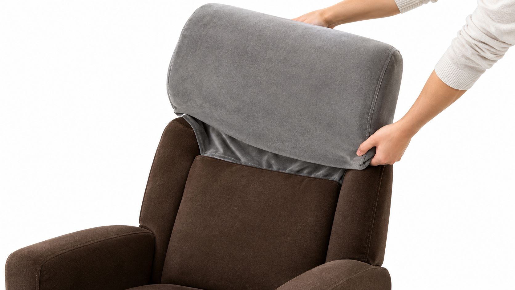 A person placing a grey stretch headrest cover onto the back of a brown armchair.