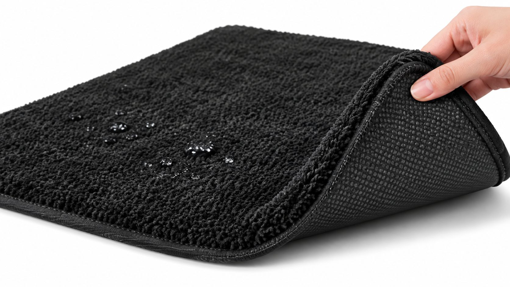 A hand lifting the corner of a black, absorbent, non-slip bathroom mat with visible water droplets.
