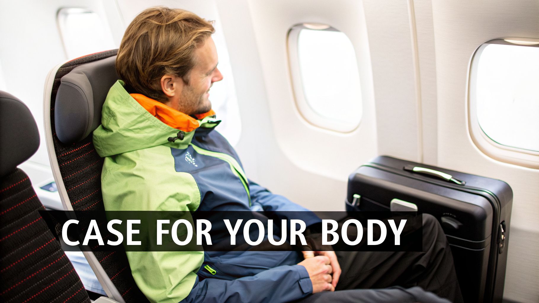 A man in a green and orange jacket sits in an airplane seat, looking out the window next to a black suitcase.