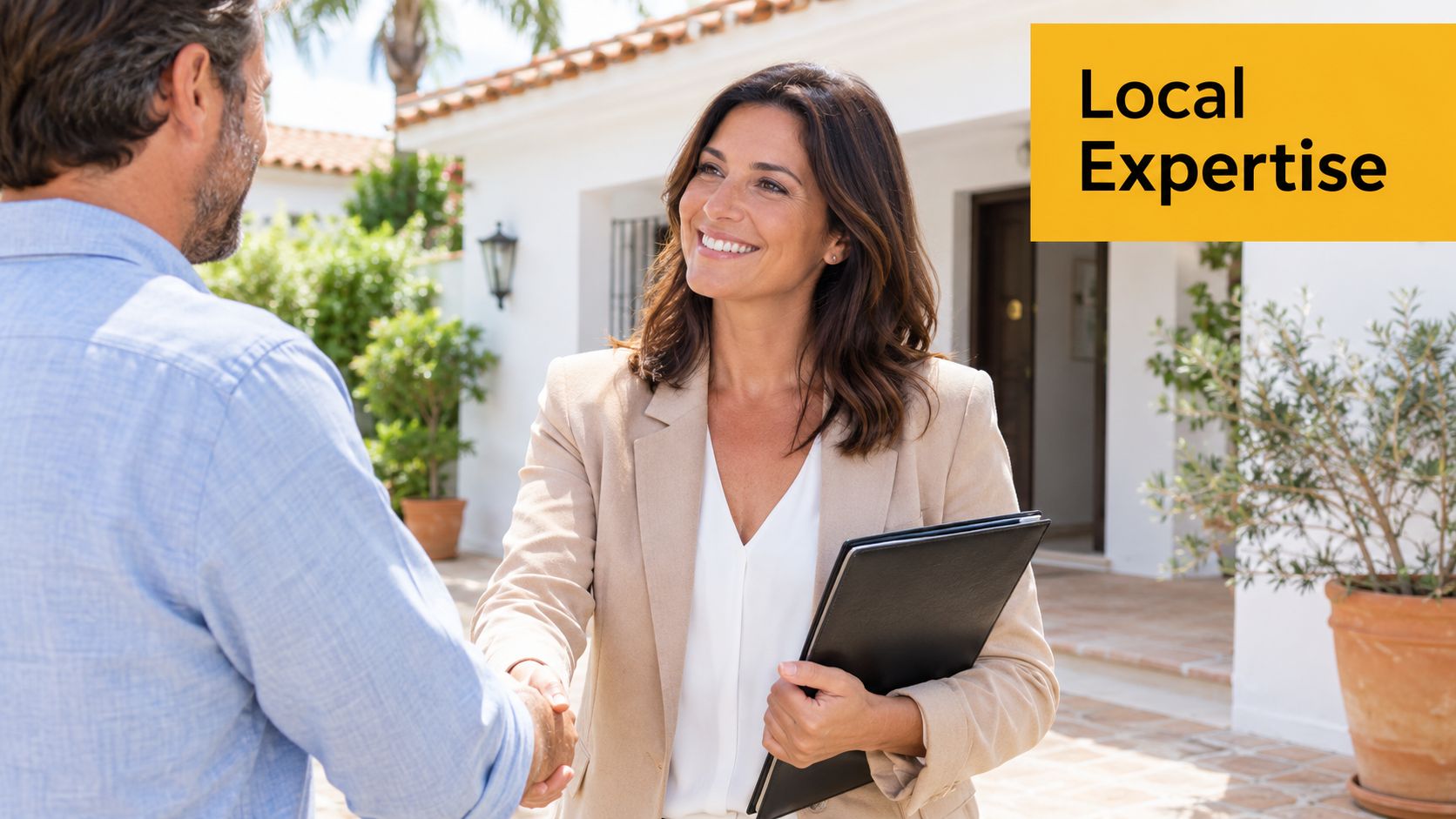 A friendly real estate agent shakes hands with a potential home buyer in front of a villa.