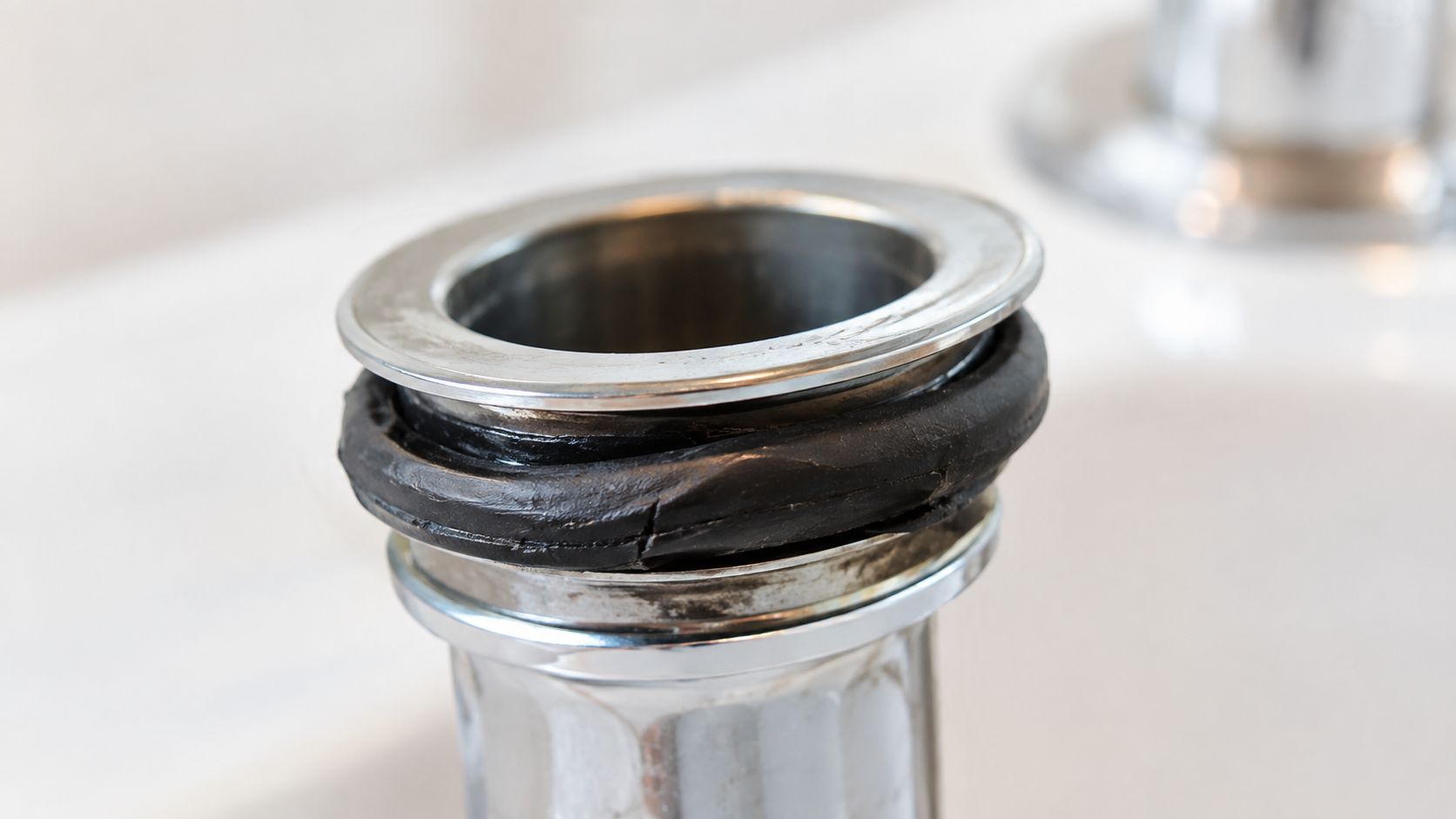 En metalbundventil til en håndvask med en beskadiget og revnet sort gummipakning monteret på toppen.