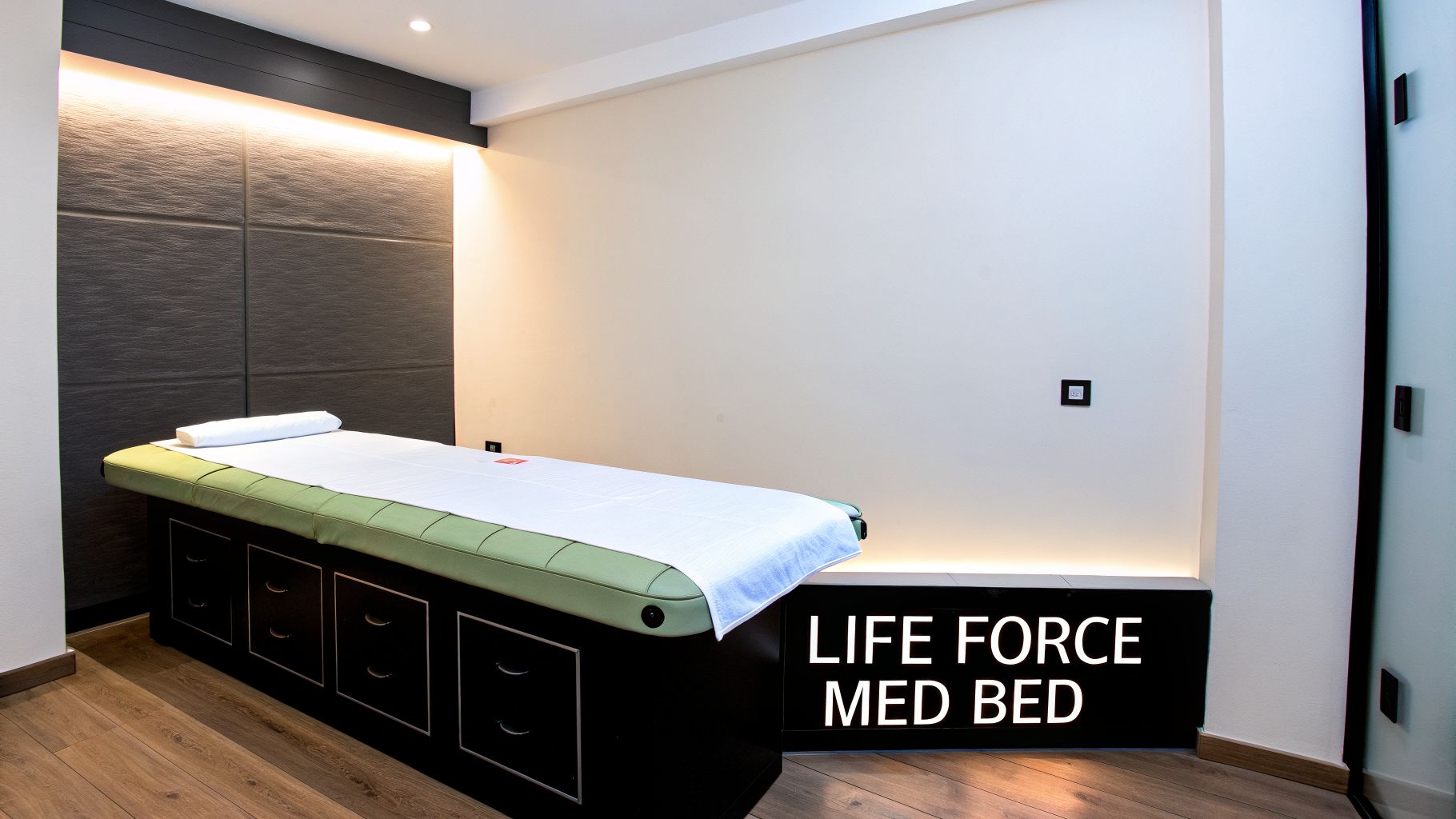 A modern medical treatment room with a green bed, white linens, and accent lighting.