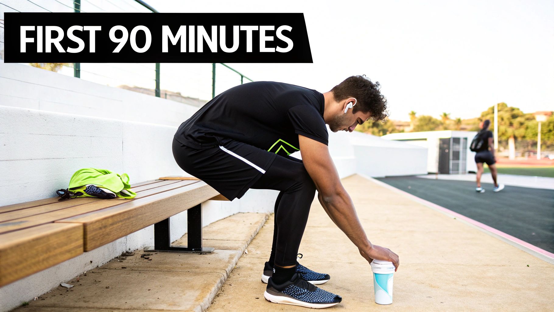 A man in athletic wear and earbuds reaches for a cup while sitting on a bench outdoors.