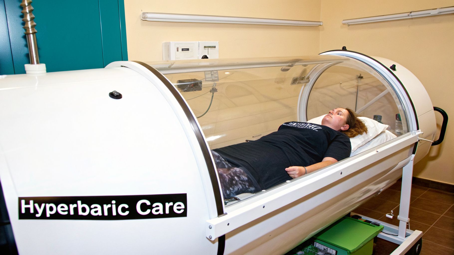 A woman lies relaxed inside a clear, white hyperbaric oxygen therapy chamber for treatment.