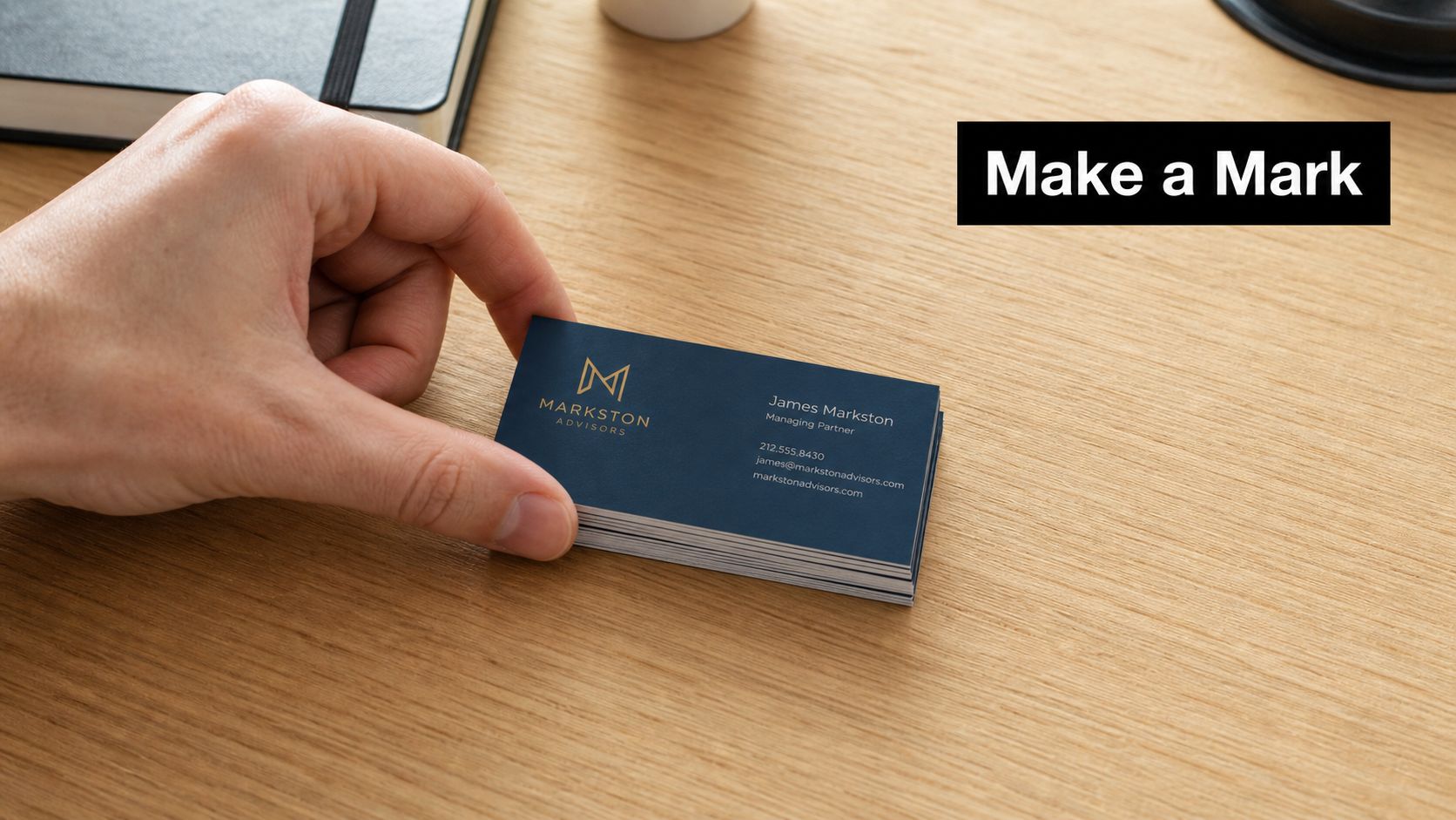 A hand holding a stack of blue business cards with gold logos on a wooden desk.