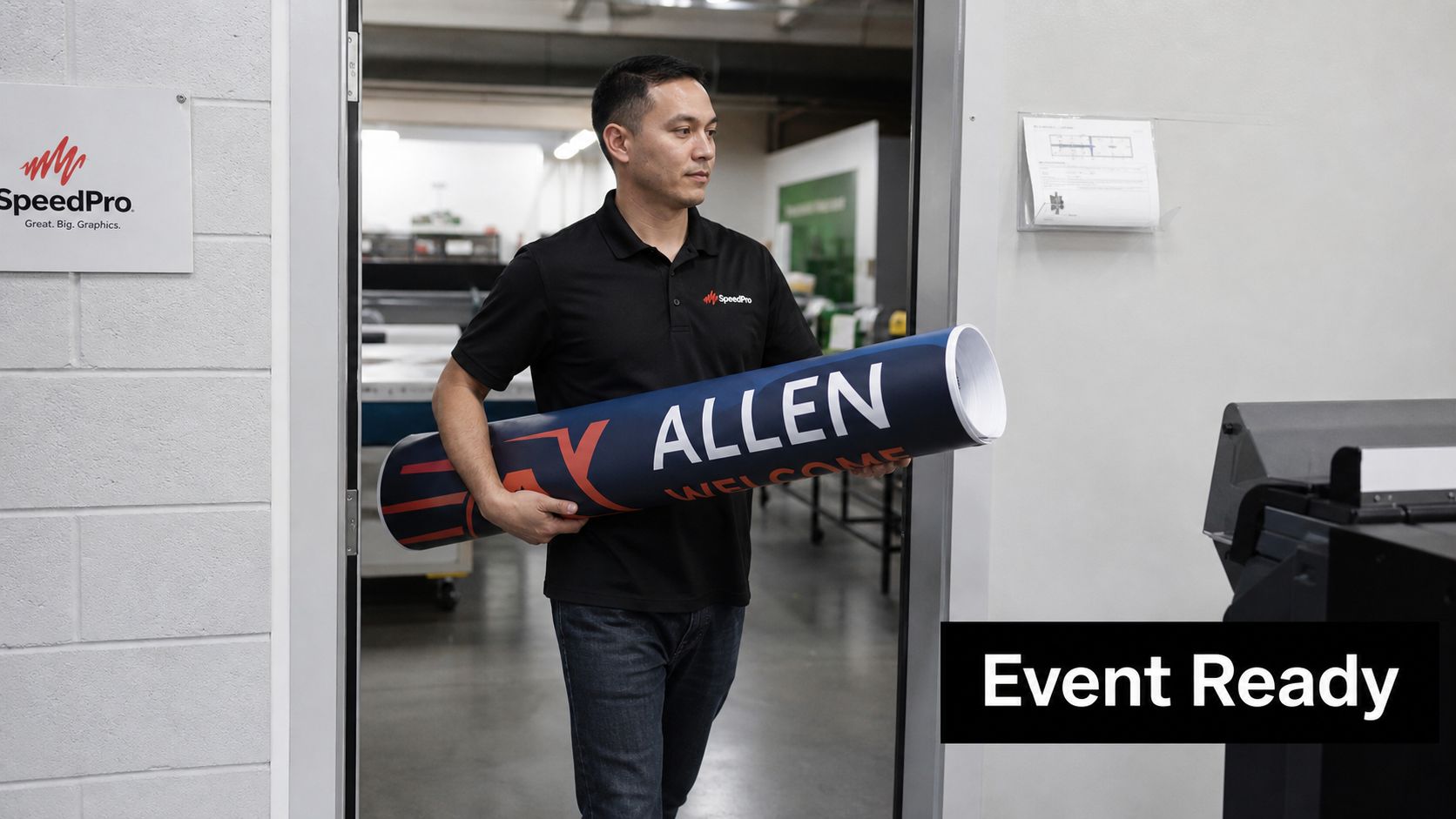 A professional holding a large rolled-up graphic banner inside a SpeedPro print production facility.