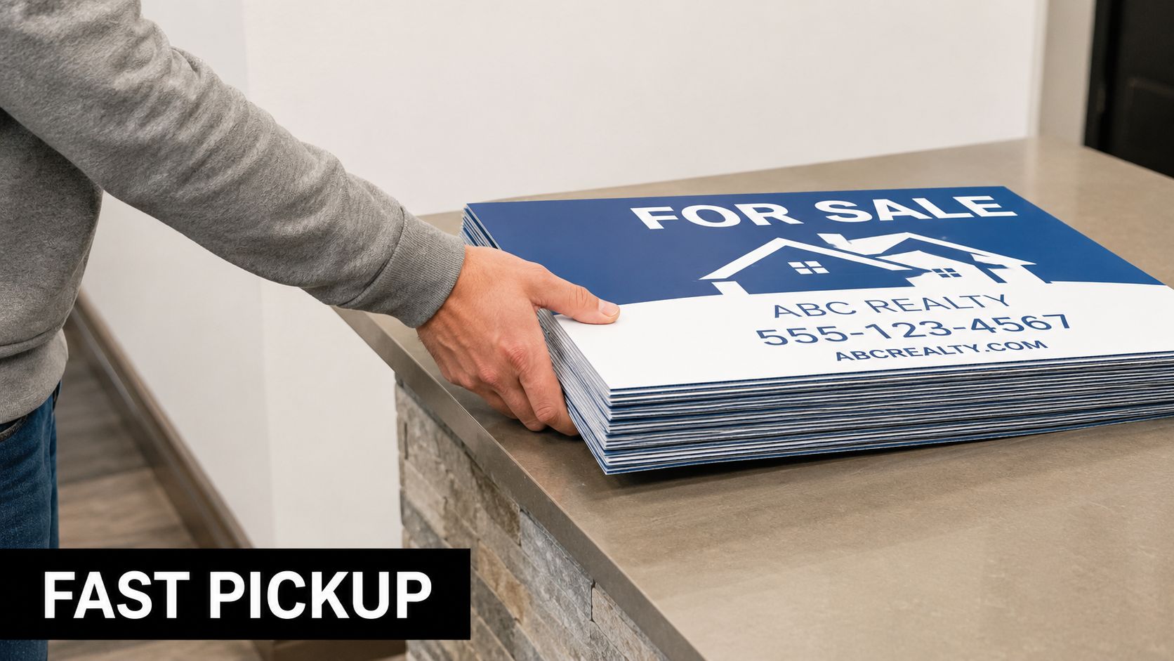 A person picking up a stack of custom printed yard signs from a counter for fast service.