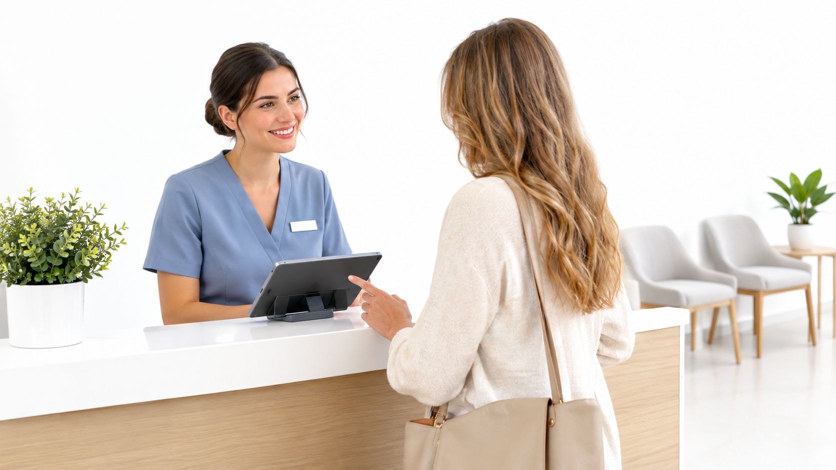 A friendly receptionist in blue scrubs assisting a patient at a modern medical office front desk.