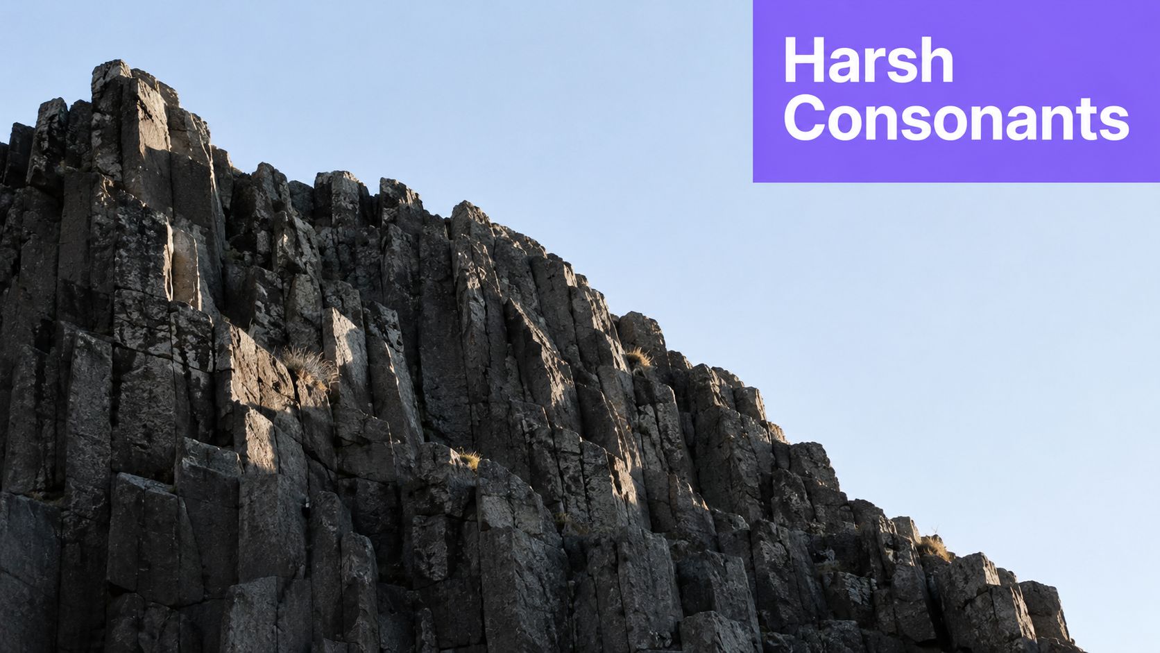 A jagged, dark basalt rock cliff formation rising against a clear, pale blue sky.