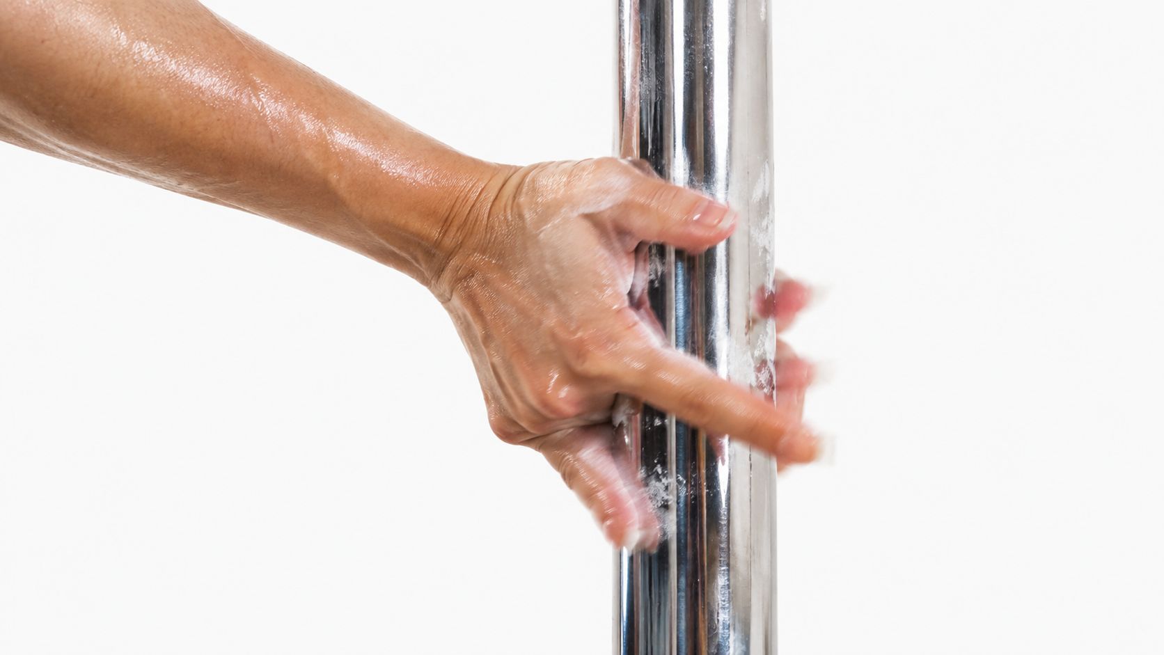 A close-up shot of a hand covered in grip chalk gripping a vertical metal pole for dancing.