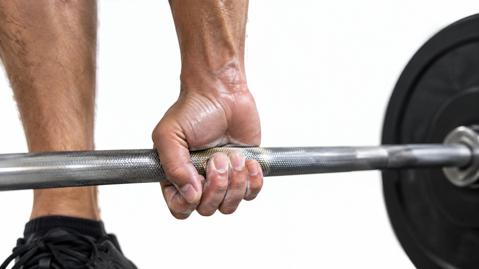 A close-up view of a person using a firm weightlifting grip on a metal barbell.