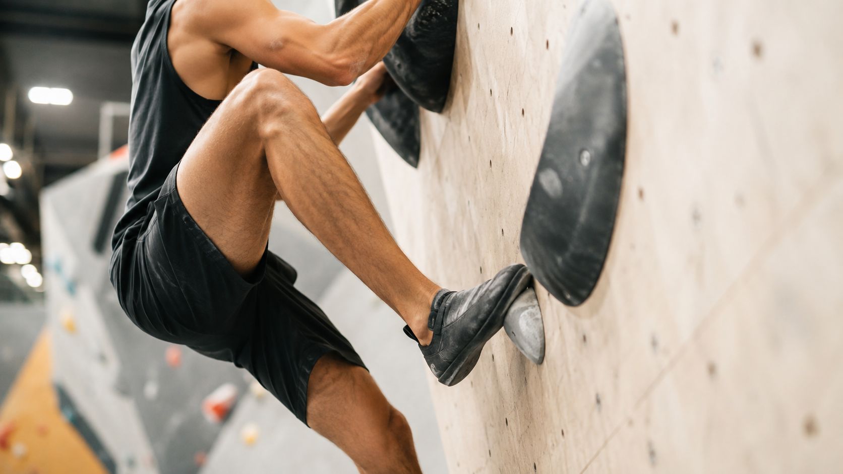 A fit male boulderer performing a challenging climbing move on an indoor gym wooden wall