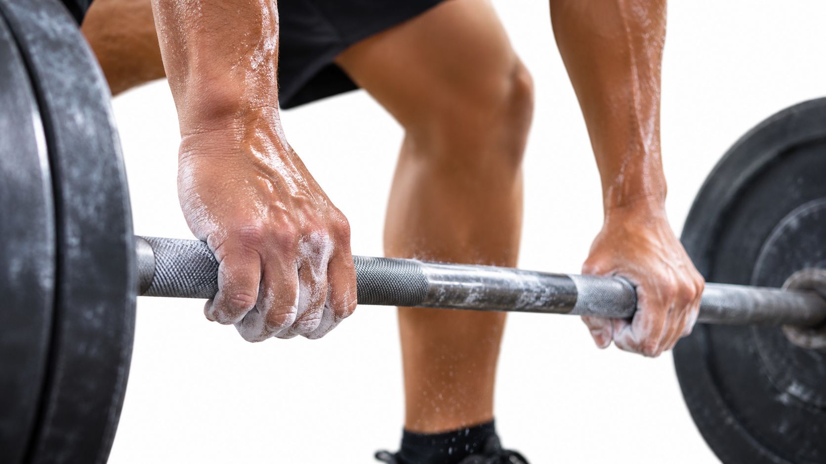 A close up view of a weightlifter gripping a barbell covered in white gymnastics chalk for training.