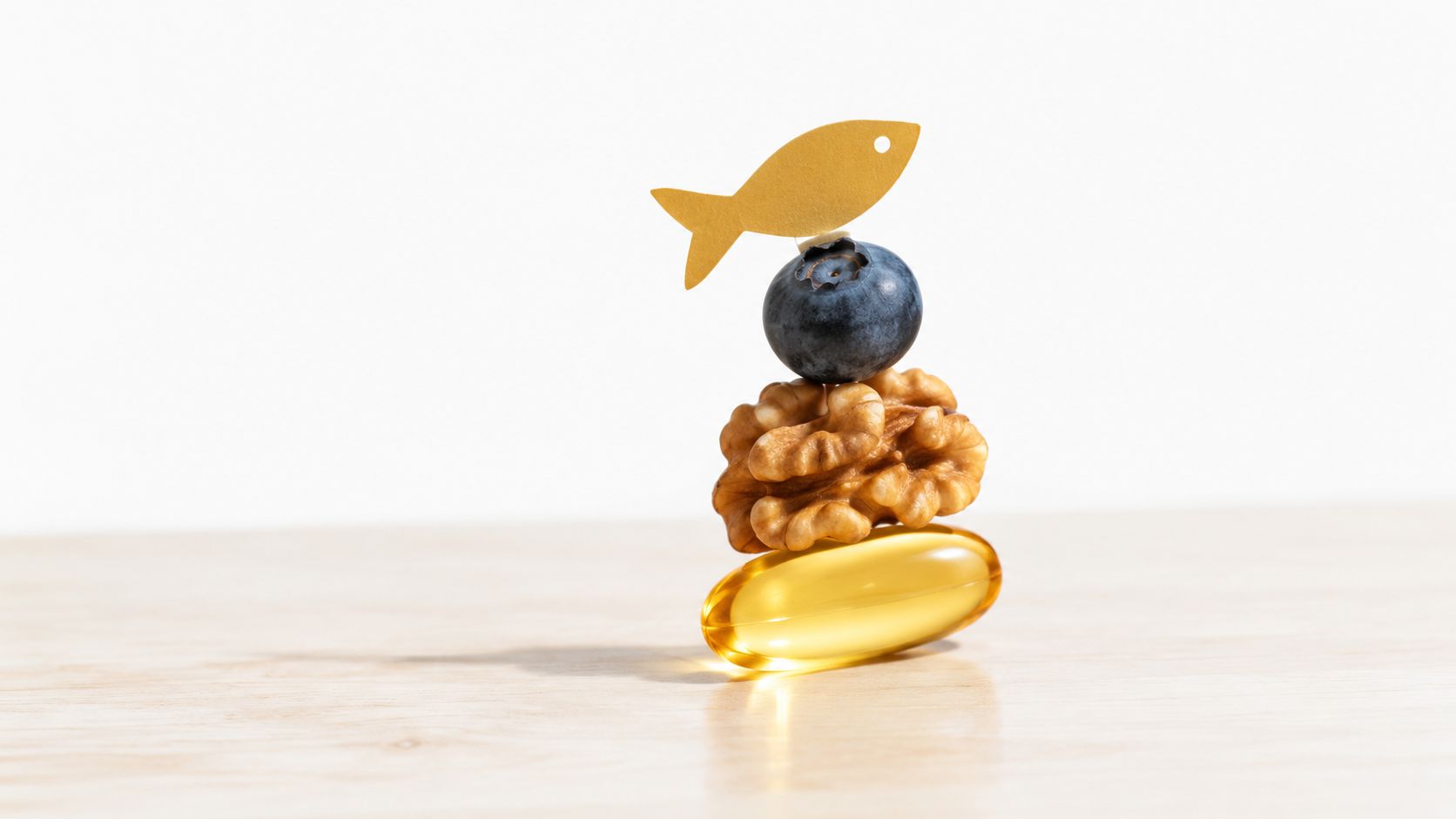 A stack consisting of a fish oil capsule, a walnut, a blueberry, and a small fish cutout.
