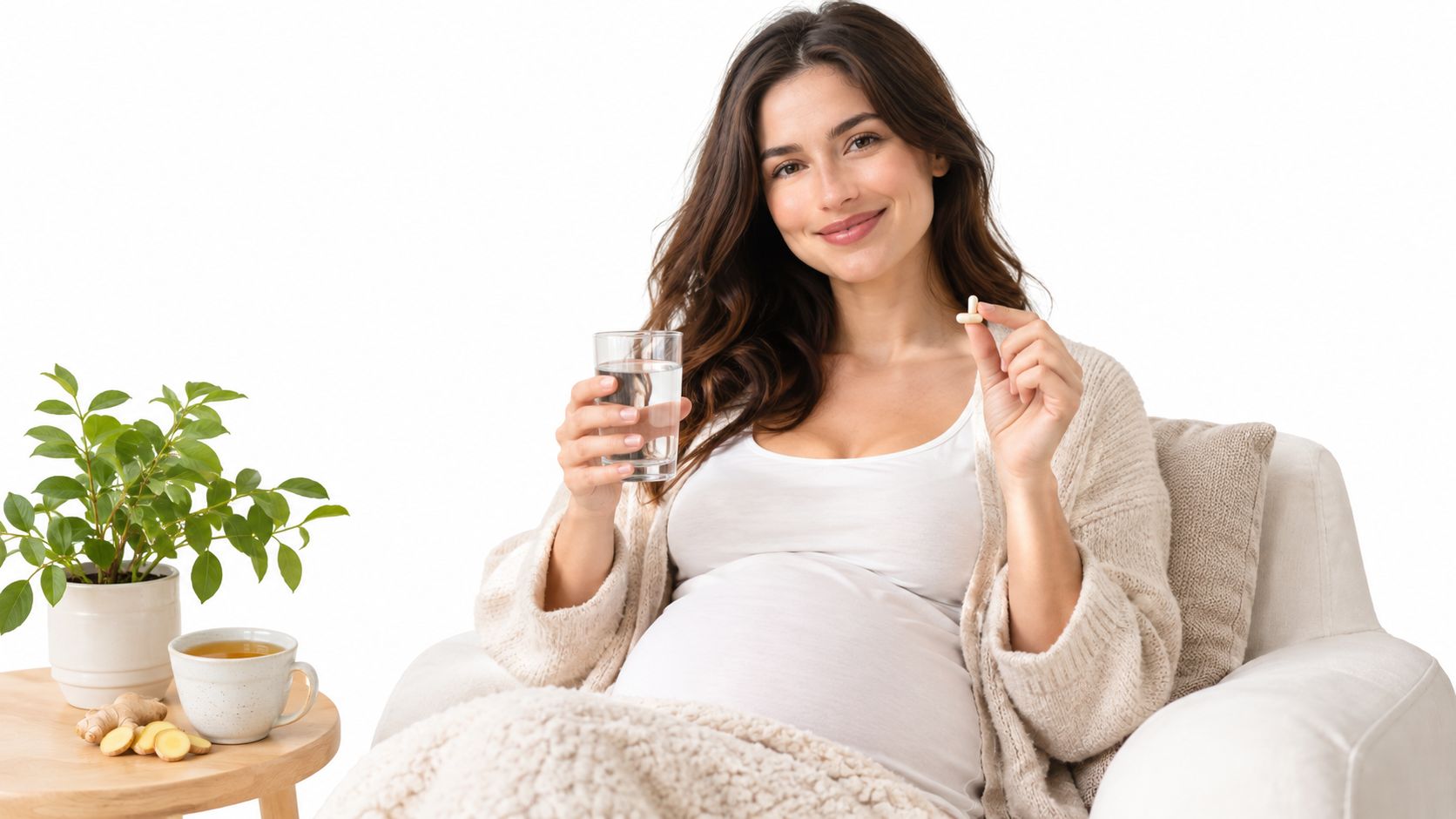 A happy pregnant woman holding a glass of water and a prenatal vitamin in a white room.