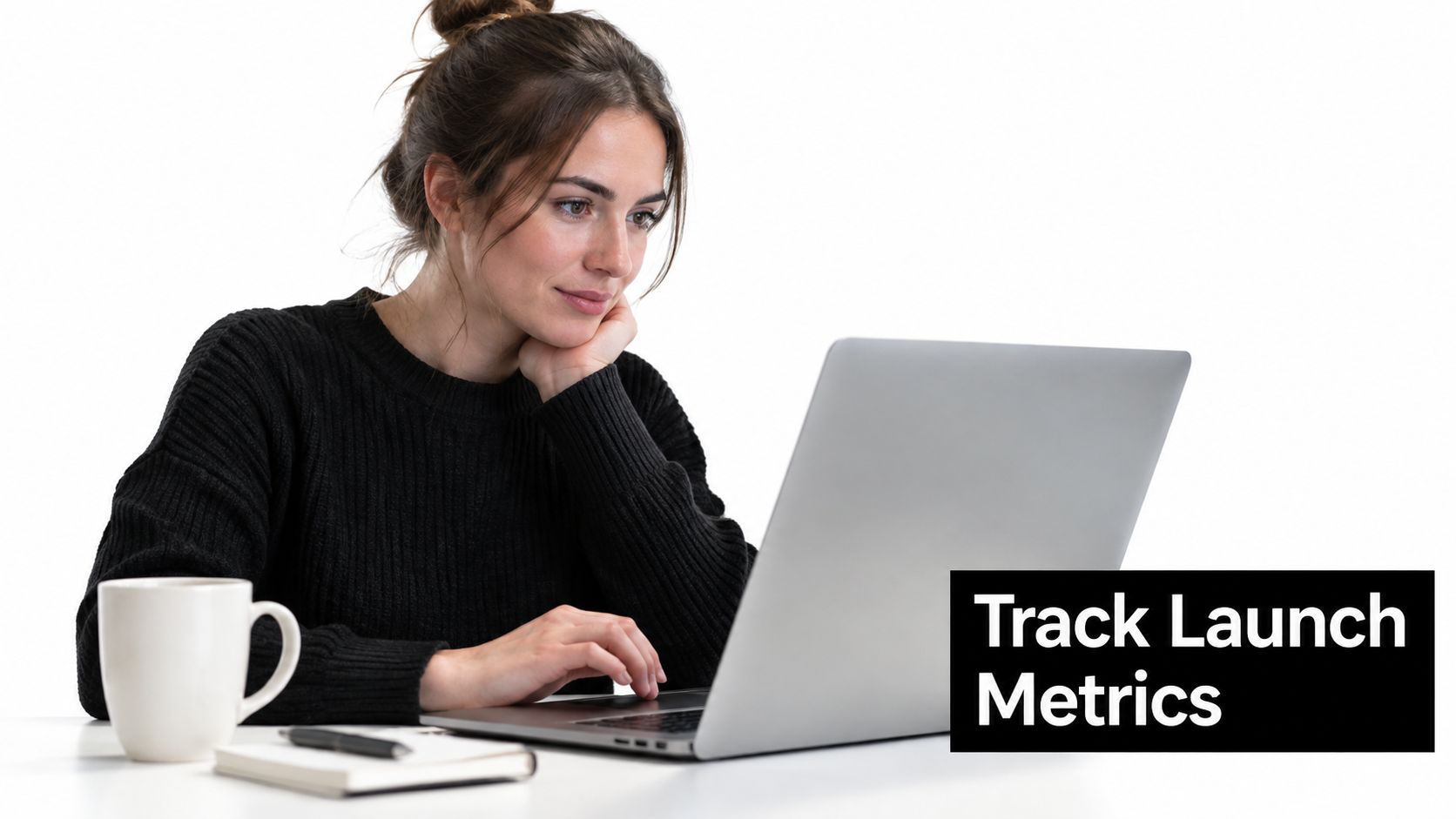 A young woman sits at a desk working on her laptop to track startup launch metrics.