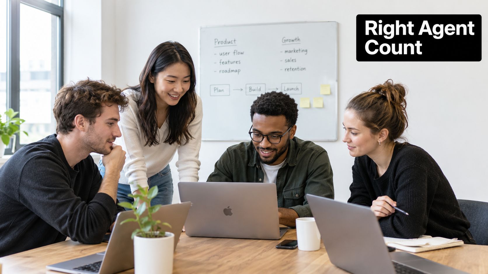 A diverse group of four young professionals collaborating on a project using laptops around a wooden office table.