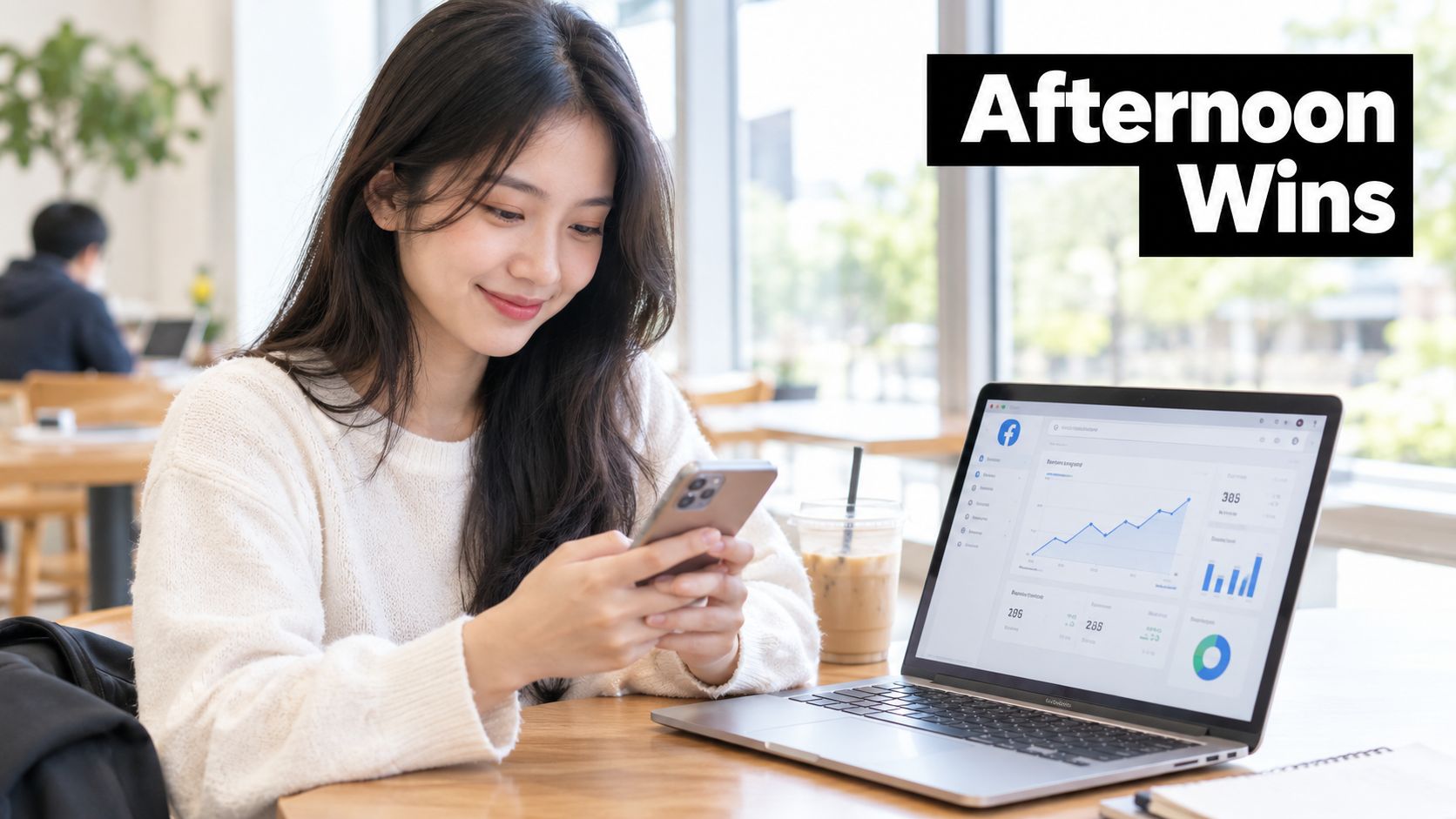 A young woman smiling while using her smartphone at a desk next to a laptop displaying analytics.
