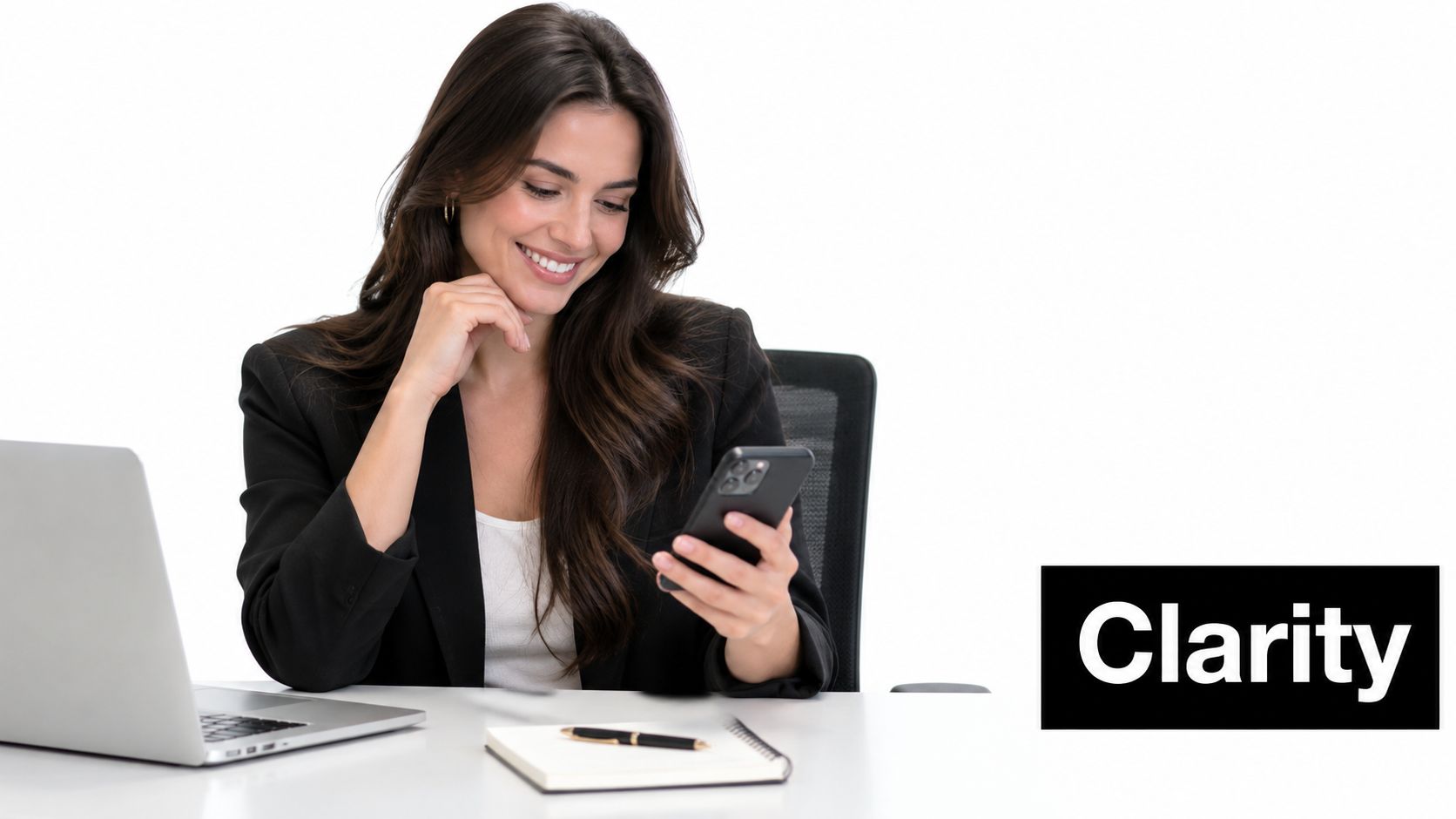A professional woman in a suit sitting at her desk using her mobile phone with a laptop
